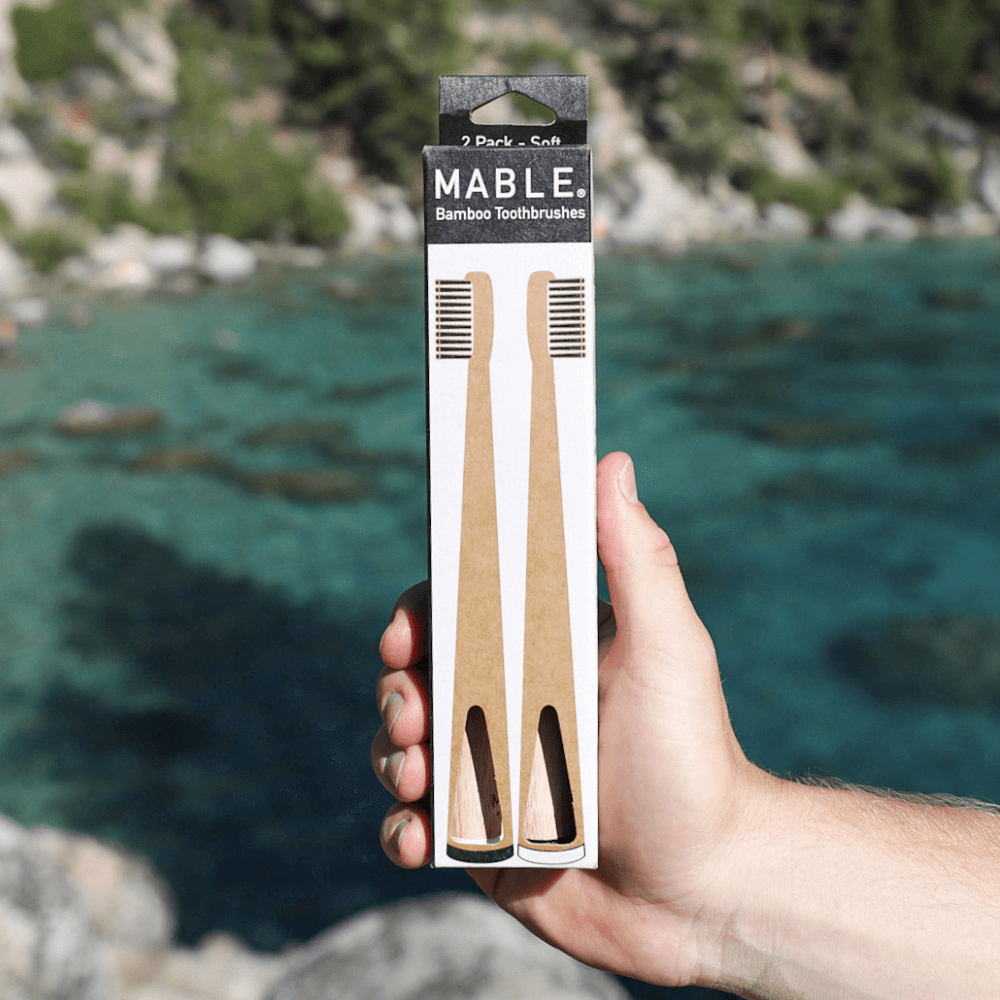 MABLE packaging is plactic-free and packages are also shipped plastic-free, Image of mans hand holding a MABLE toothbrush two pack made from recyclable cardboard packaging