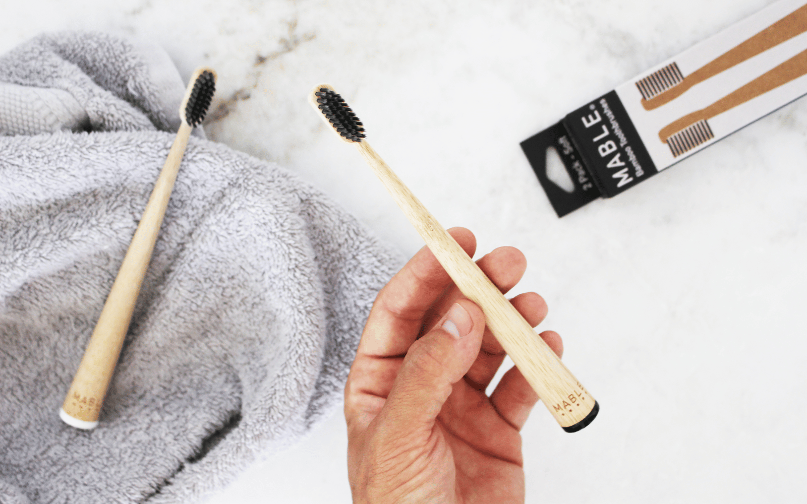 MABLE bamboo toothbrush in an adult charcoal pack. Mans hand holding a black bamboo toothbrush with charcoal infused bristles. 